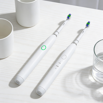 Two white Rotating Electric Toothbrush | PA3618 models with blue and green bristles on a light wood surface next to cups and a glass of water