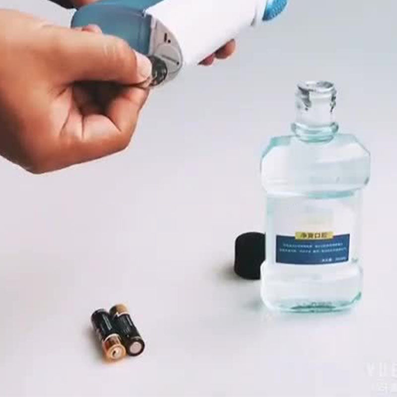 Hand inserting batteries into Electric Water Flosser | PA5338 with mouthwash bottle nearby on white surface